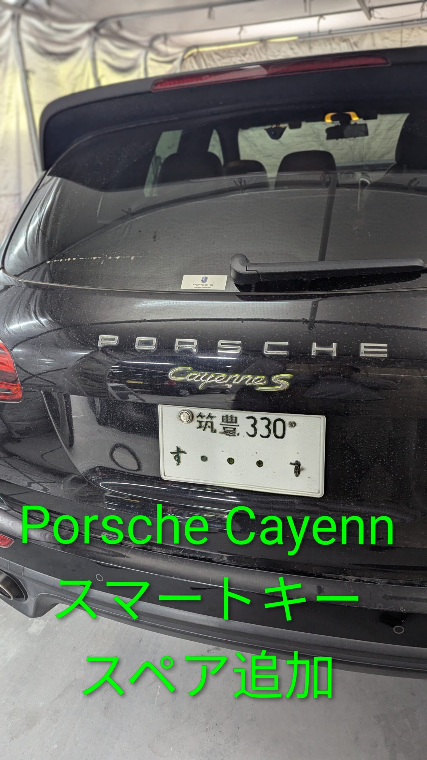 Rear view of a black Porsche Cayenne S with a Japanese license plate, parked inside a garage or tented area.