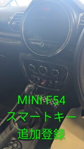 MINI F54 interior: circular center touchscreen, climate controls, and gear shifter; bright green Japanese text overlay readout in foreground.