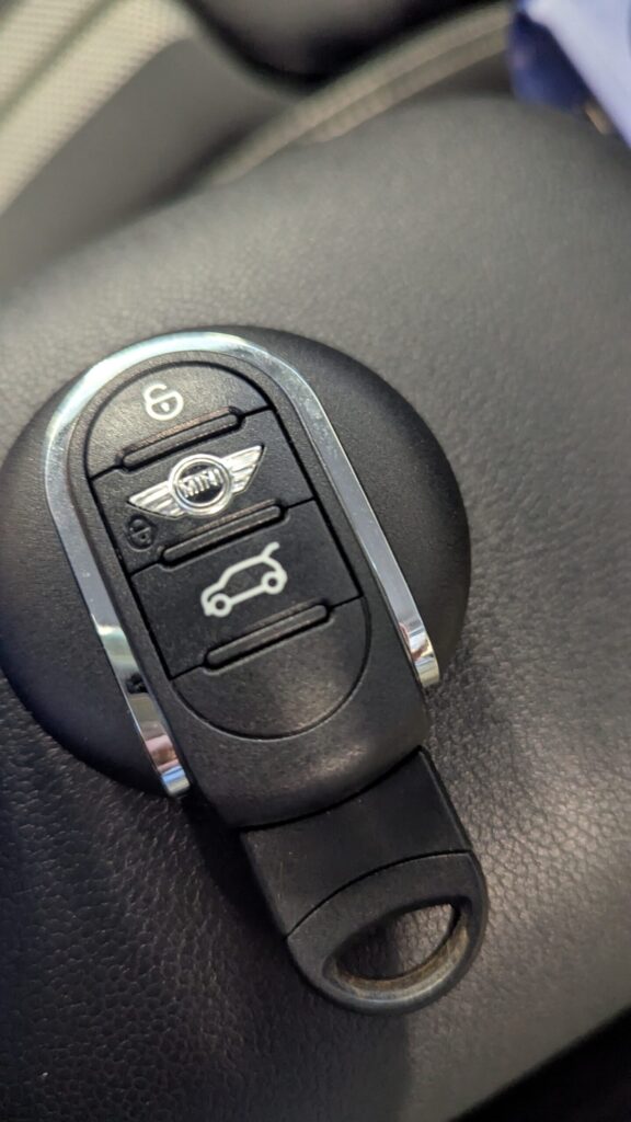 Close-up of a MINI car key fob on a dark surface, showing lock and trunk-release buttons with the MINI emblem in the center. - 車専門鍵店カーロック 施工実績・鍵作成