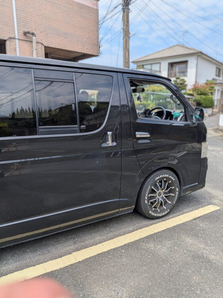 Black van parked along a street with the front door window open; houses and power lines visible in the background. - 車専門鍵店カーロック 施工実績・鍵作成